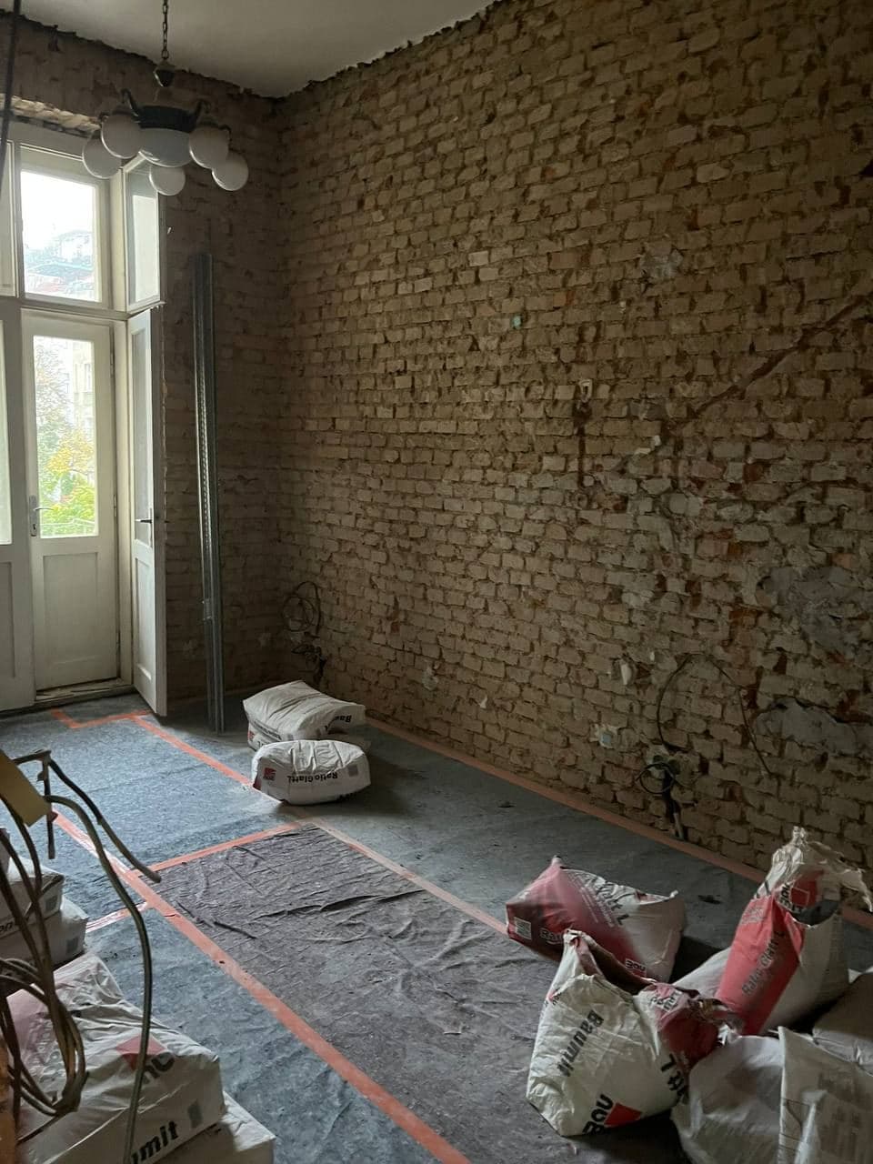 Pokoj vybouraný až na cihelné zdivo, podlaha zakrytá ochrannou textilií