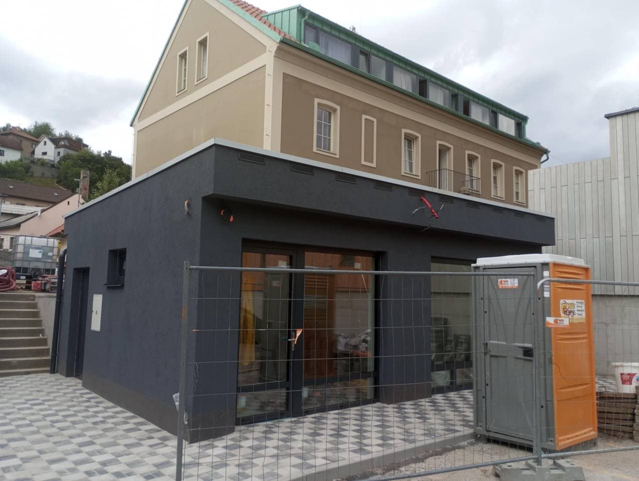 Dokončený obchodní prostor s tmavou fasádou, proskleným vstupem a dlažbou.