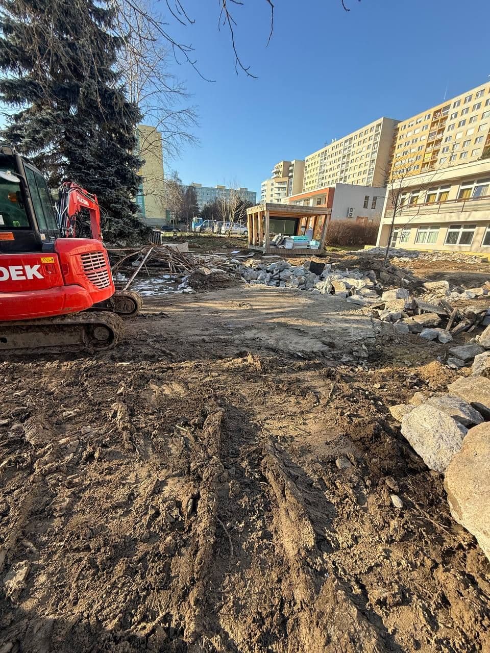 Terénní úpravy kolem objektu: pásové rypadlo odtěžuje rozbitou plochu u budovy.