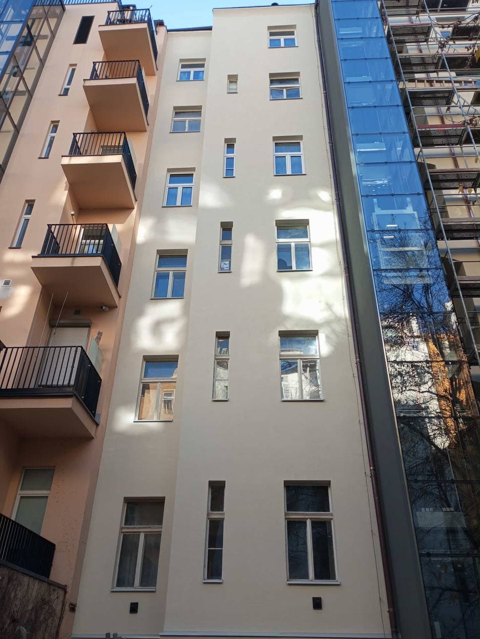 Obnovená světlá dvorní fasáda vícepodlažního domu.